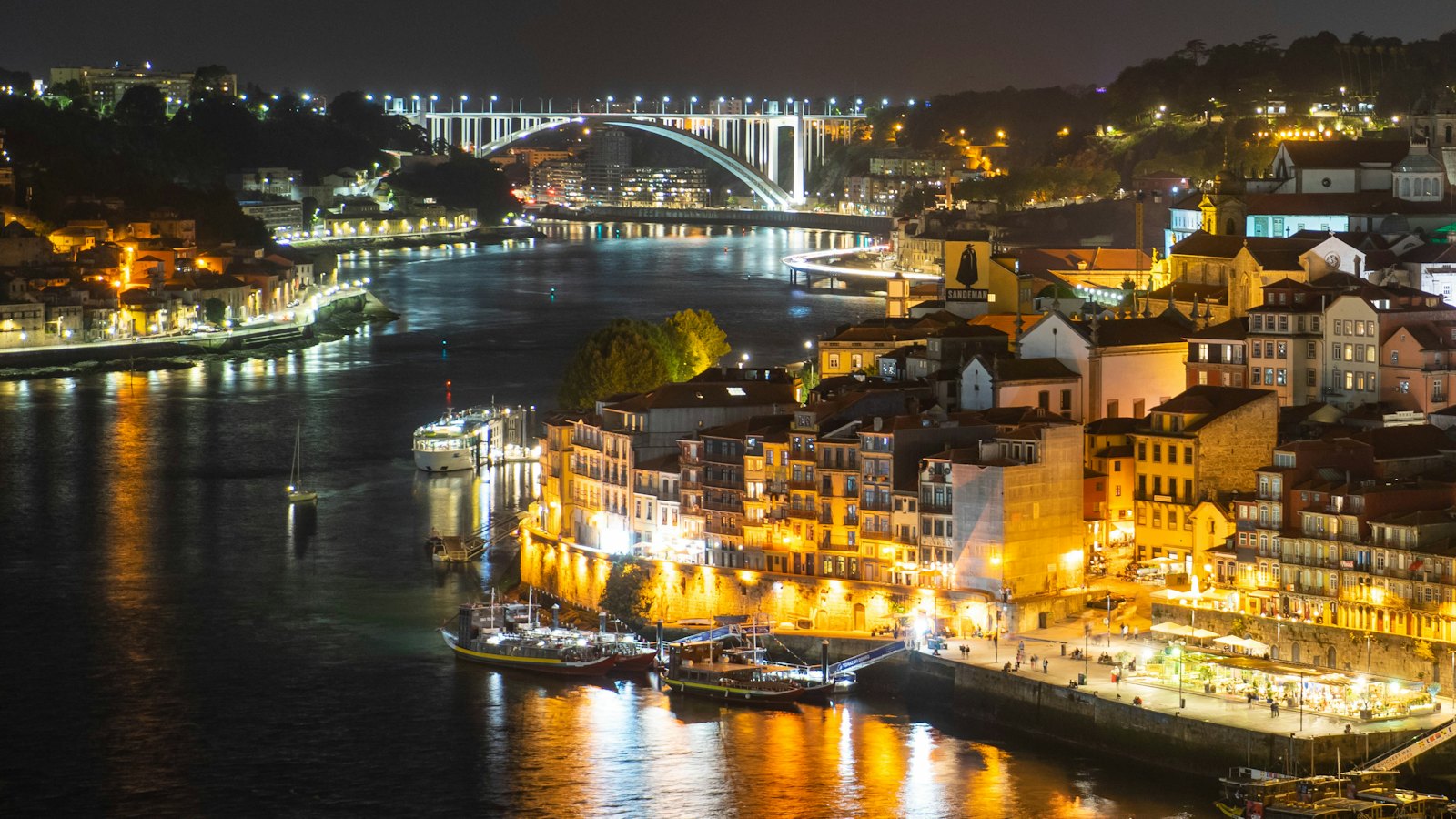 Dom Luis bridge arching over the illuminated Ribeira riverfront in Porto at night