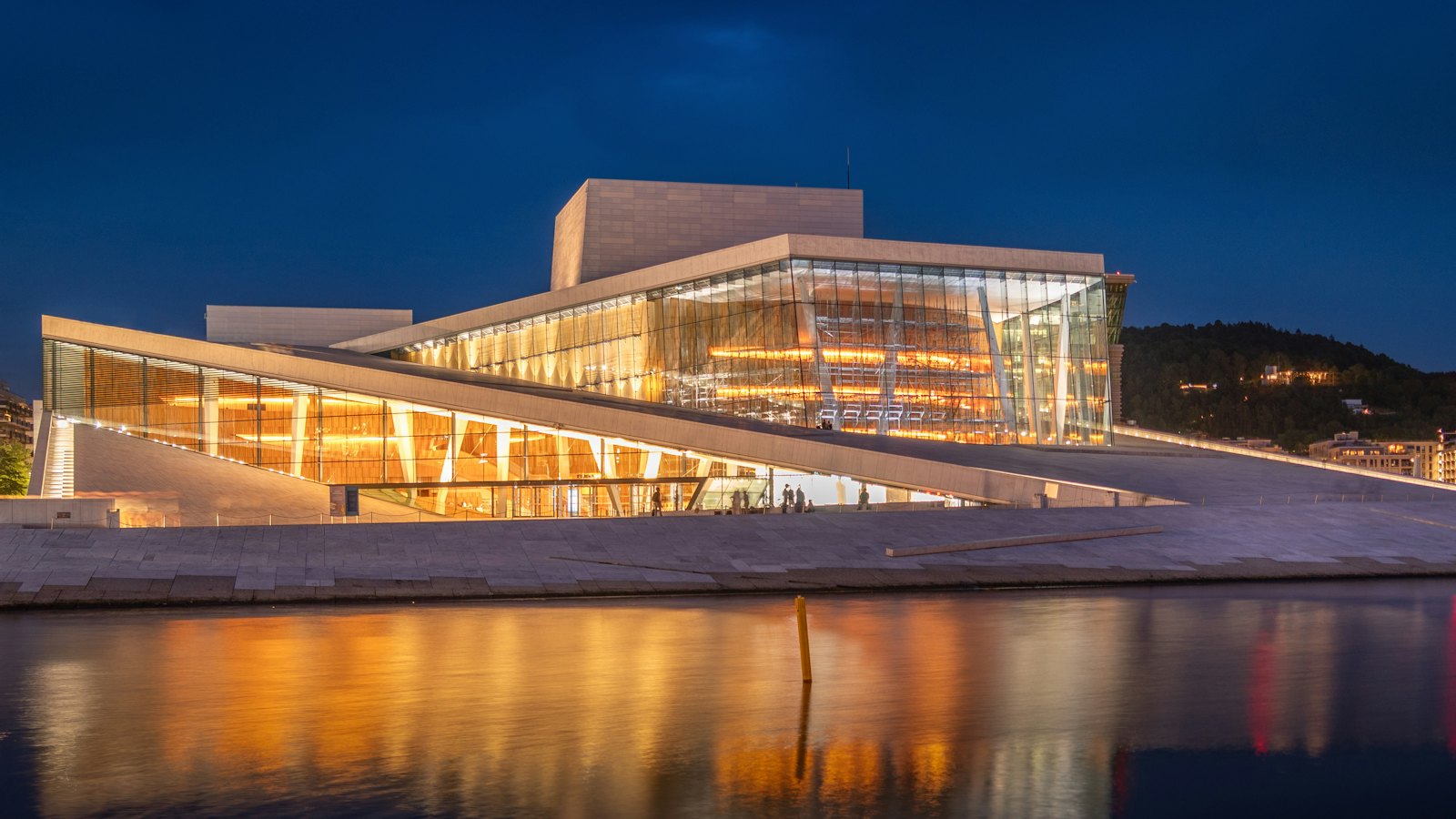Oslo Opera House's angular white roof illuminated and reflected in the water at blue hour