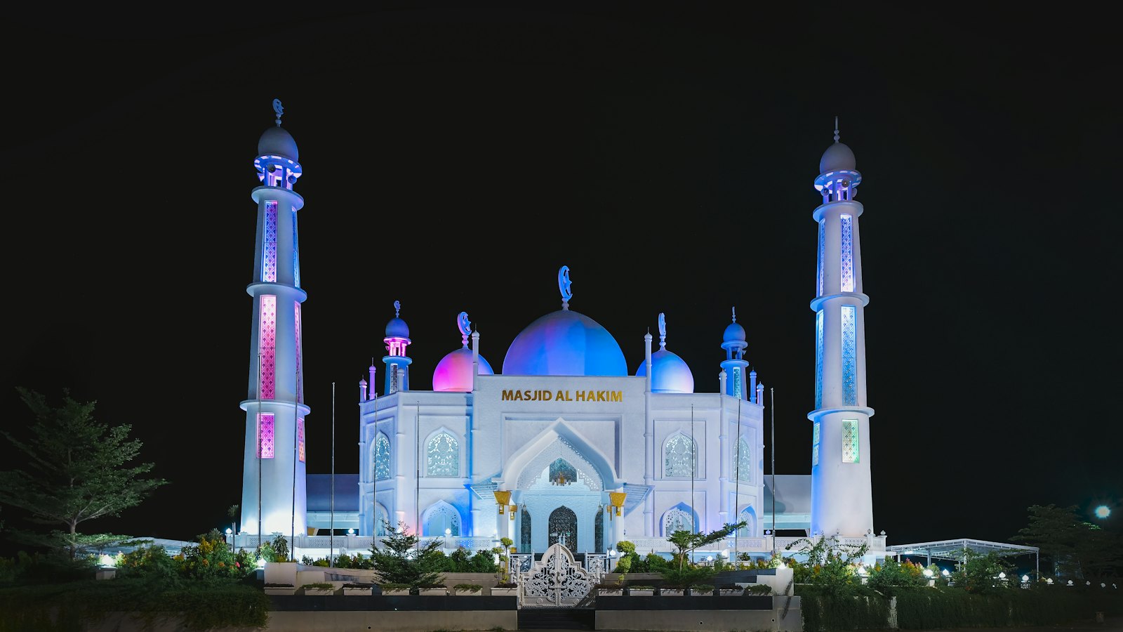 Masjid Al Hakim on the Padang seafront, its white domes and minarets lit blue at night
