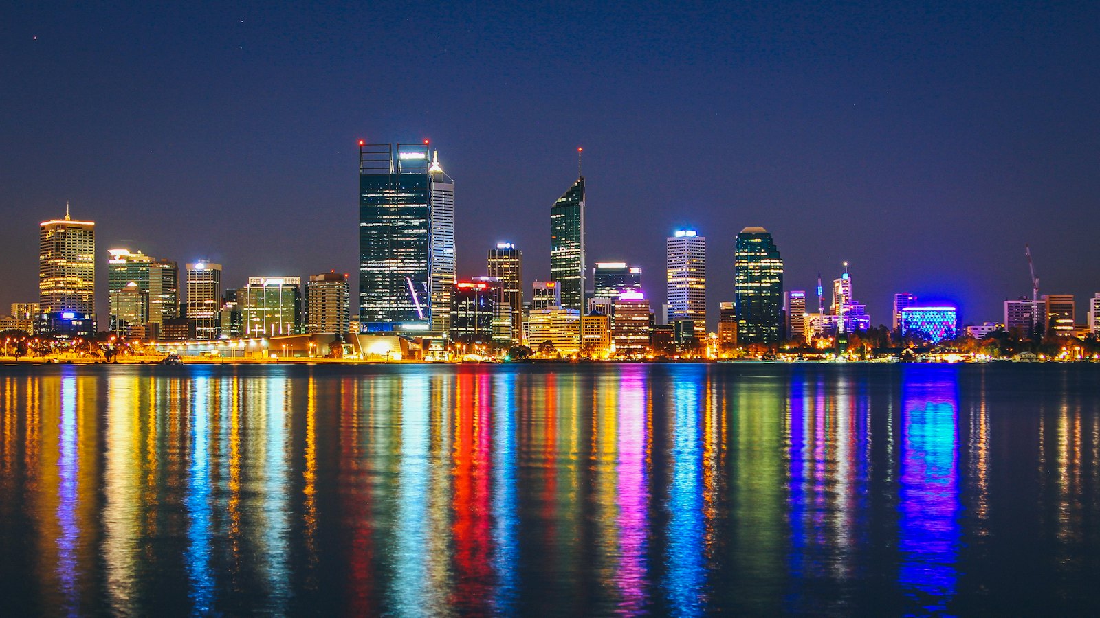 Perth city skyline lit up at night, reflected in colourful streaks across the Swan River