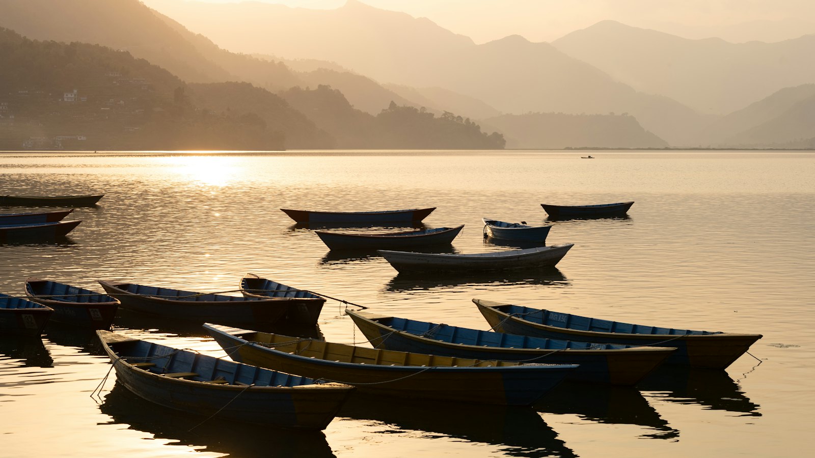 Wooden rowboats silhouetted on golden misty Phewa Lake at dusk in Pokhara