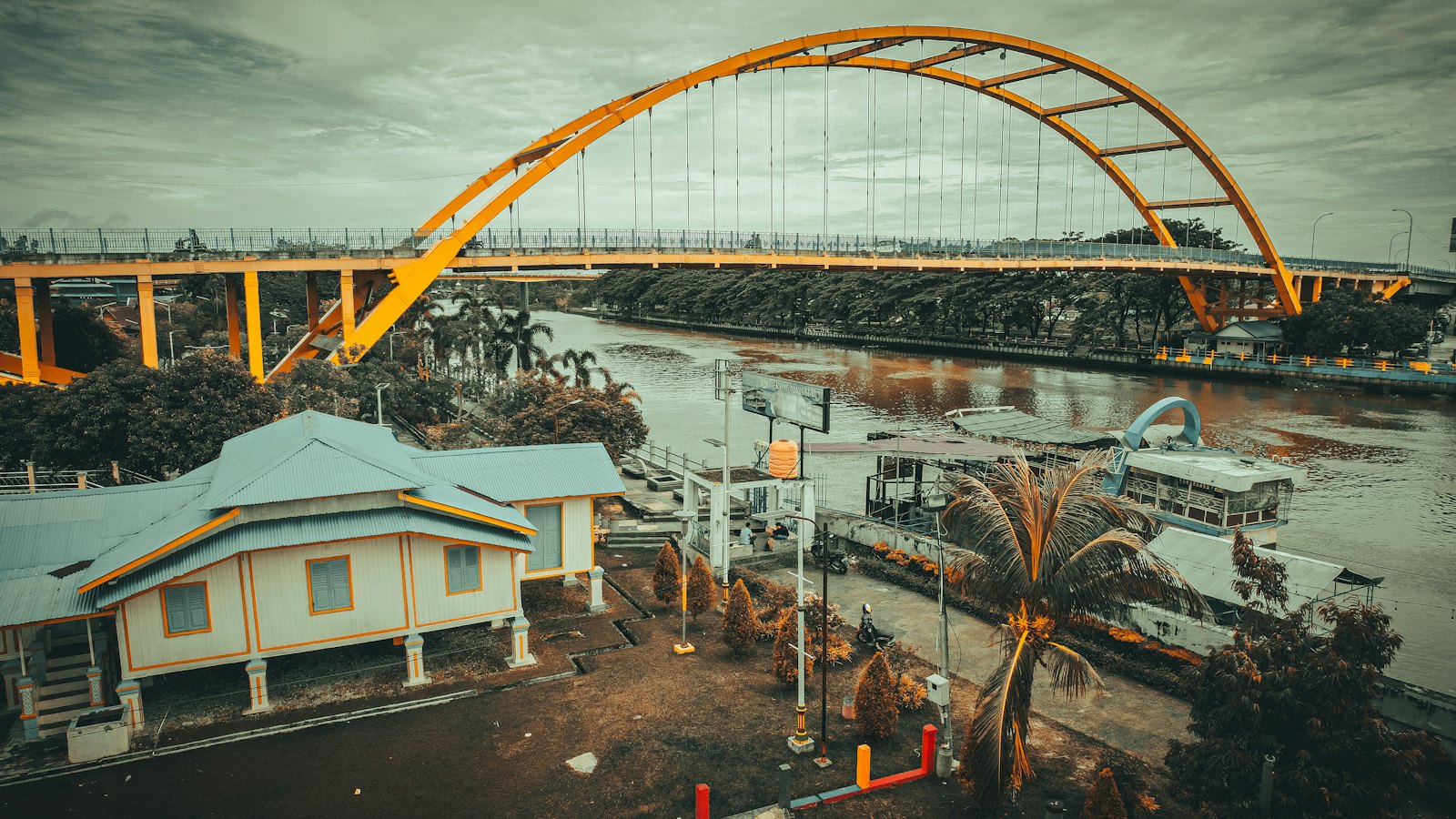 Orange steel arch bridge over the Siak River beside a historic building in Pekanbaru