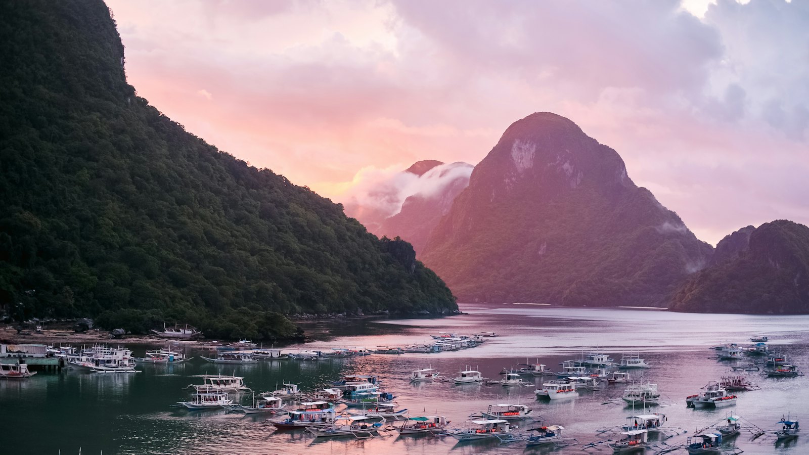 Bangka boats moored in Bacuit Bay, El Nido, Palawan, below limestone karst peaks at pink dusk