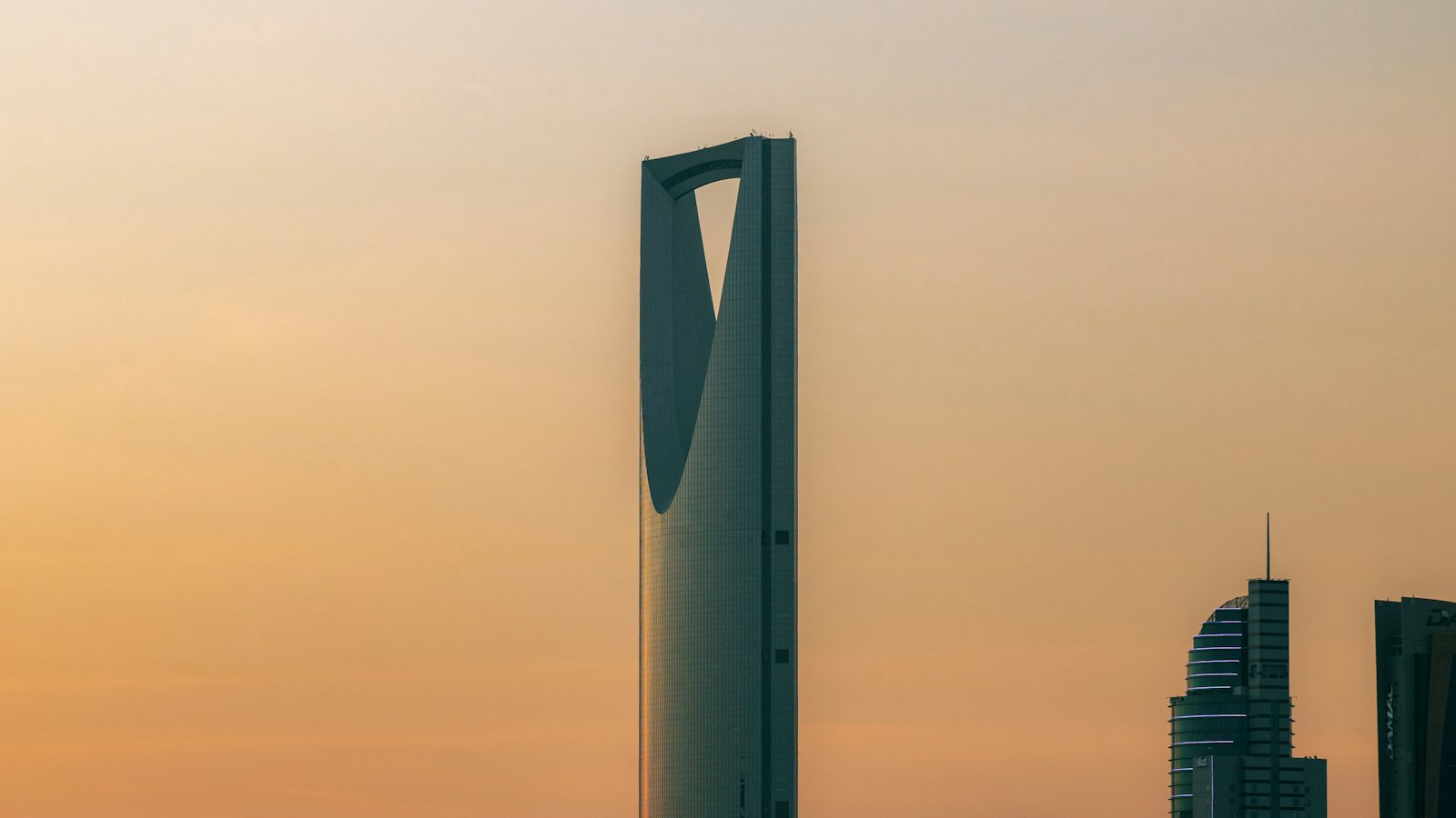 Kingdom Centre Tower's arched crown silhouetted against an orange sunset sky in Riyadh