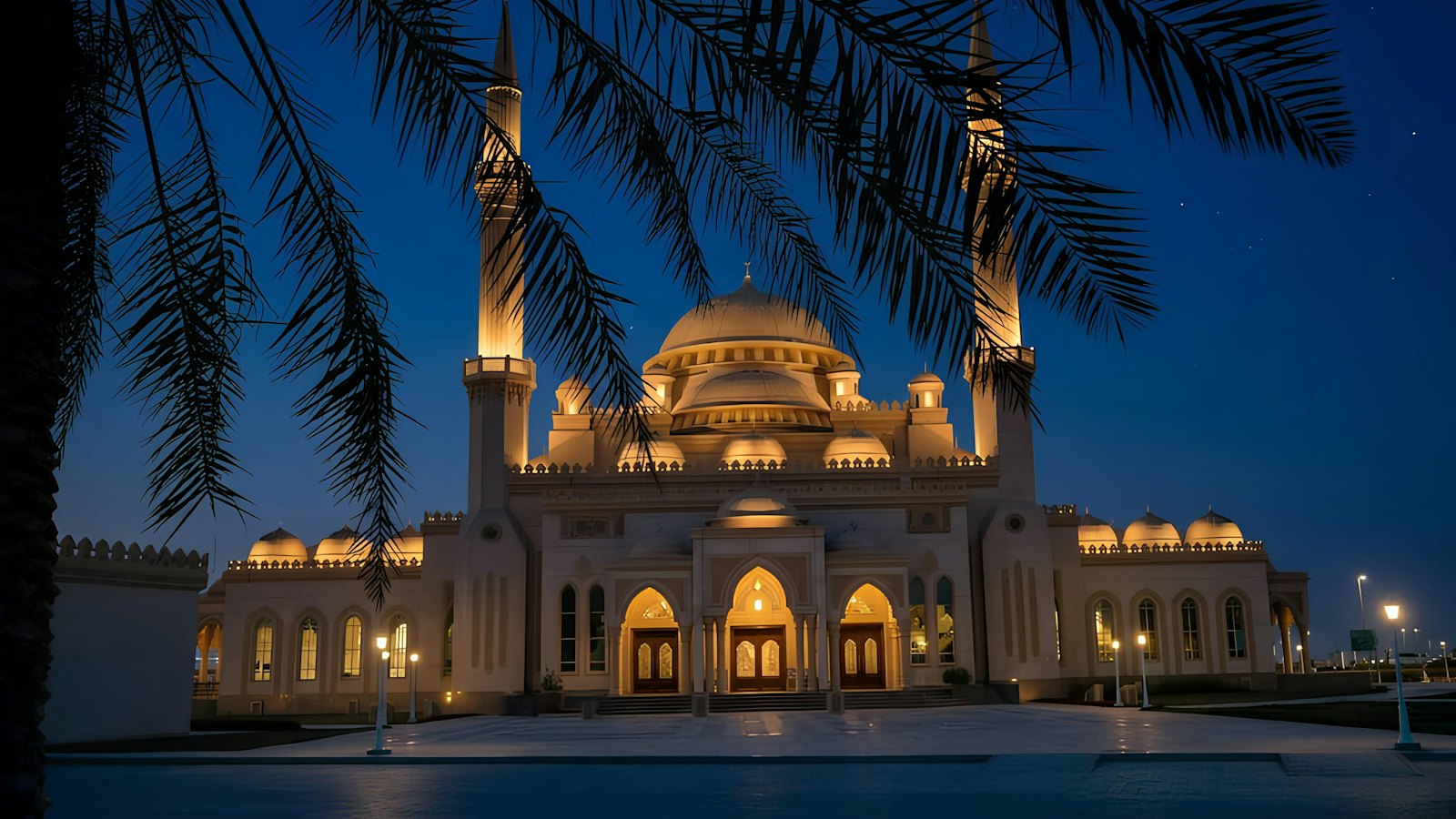 Illuminated domed mosque with twin minarets framed by palm trees at night in Sharjah