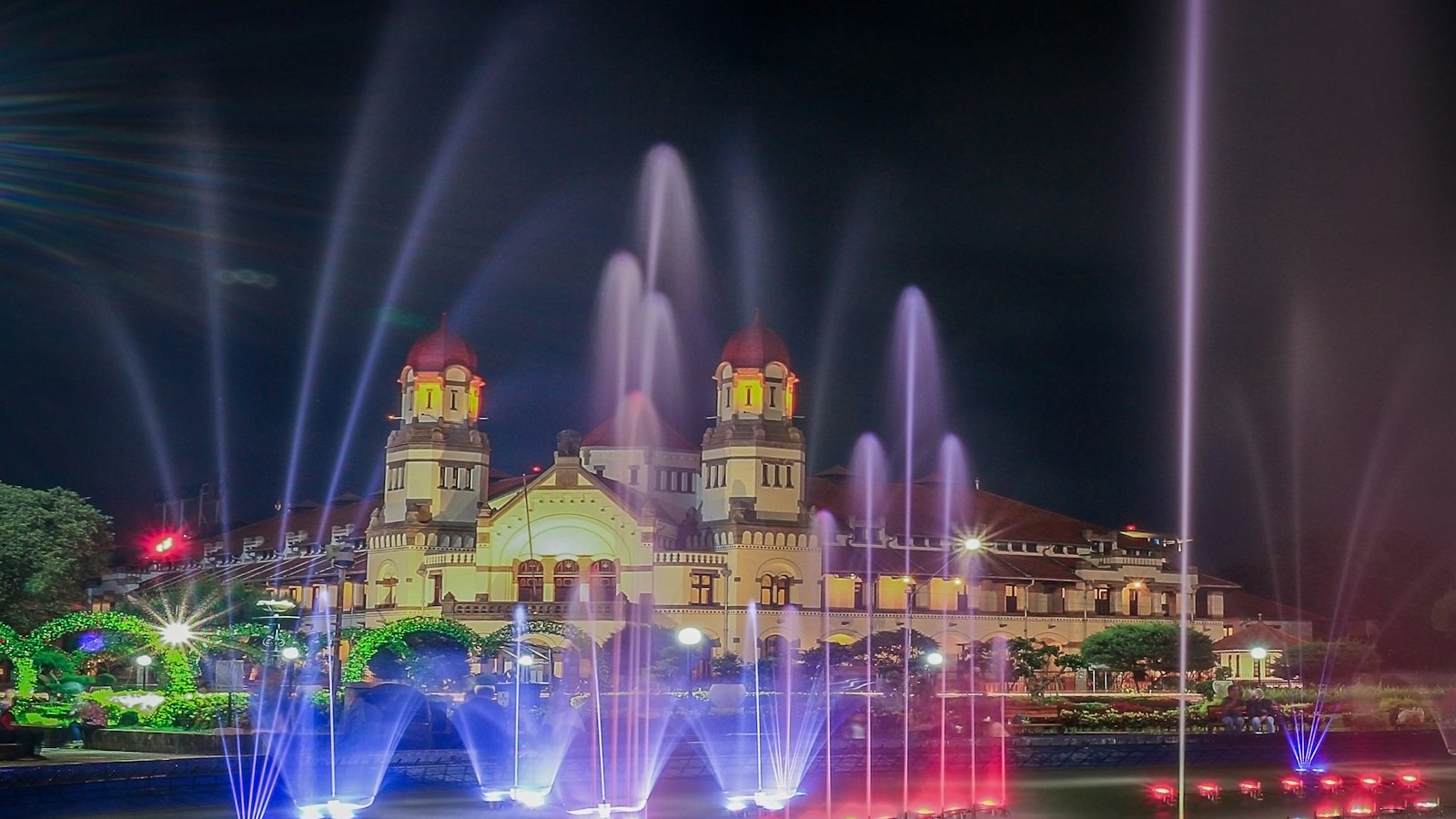 Illuminated fountains dance before the historic Lawang Sewu building at night in Semarang