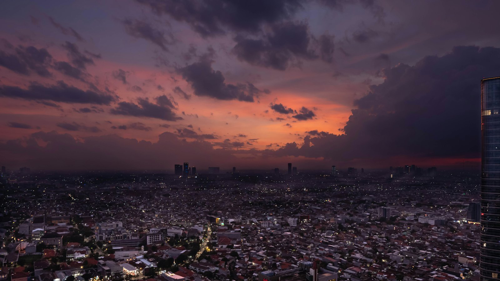 Dusk over Surabaya, East Java, with city lights glowing beneath a fiery orange and purple sky