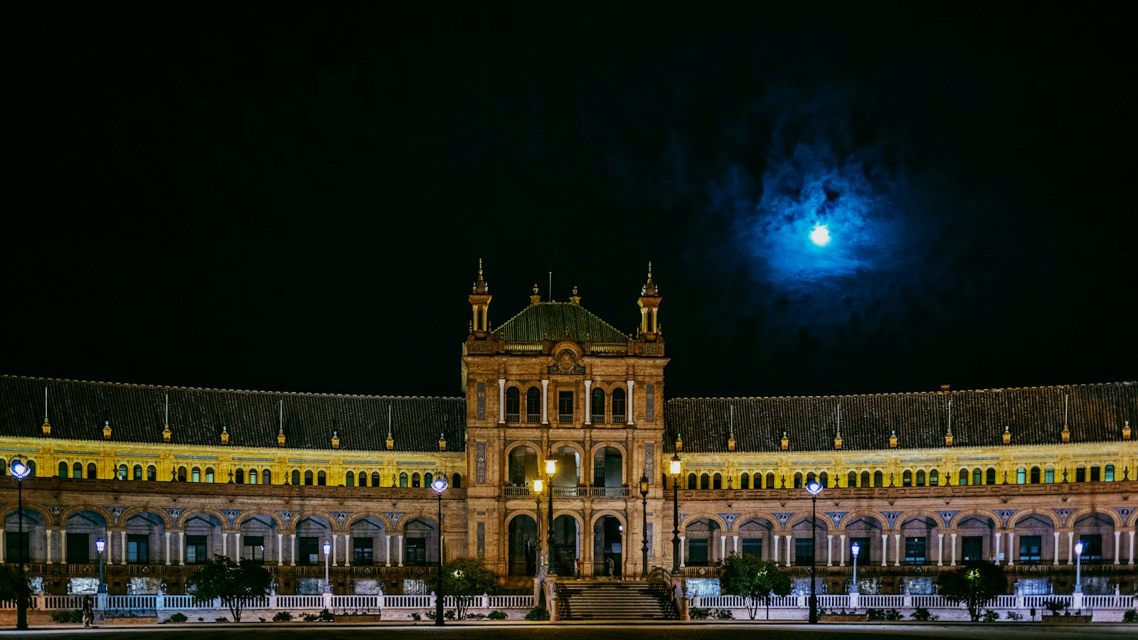 Plaza de Espana's grand facade lit up at night under a full moon