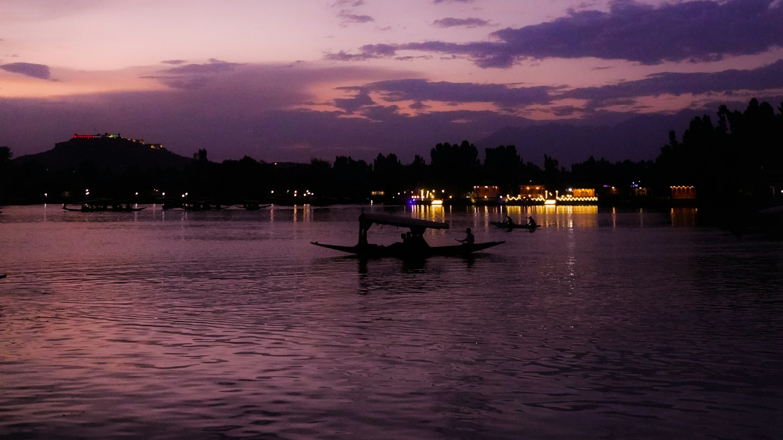 A shikara boat glides across Dal Lake beneath a violet dusk sky in Srinagar