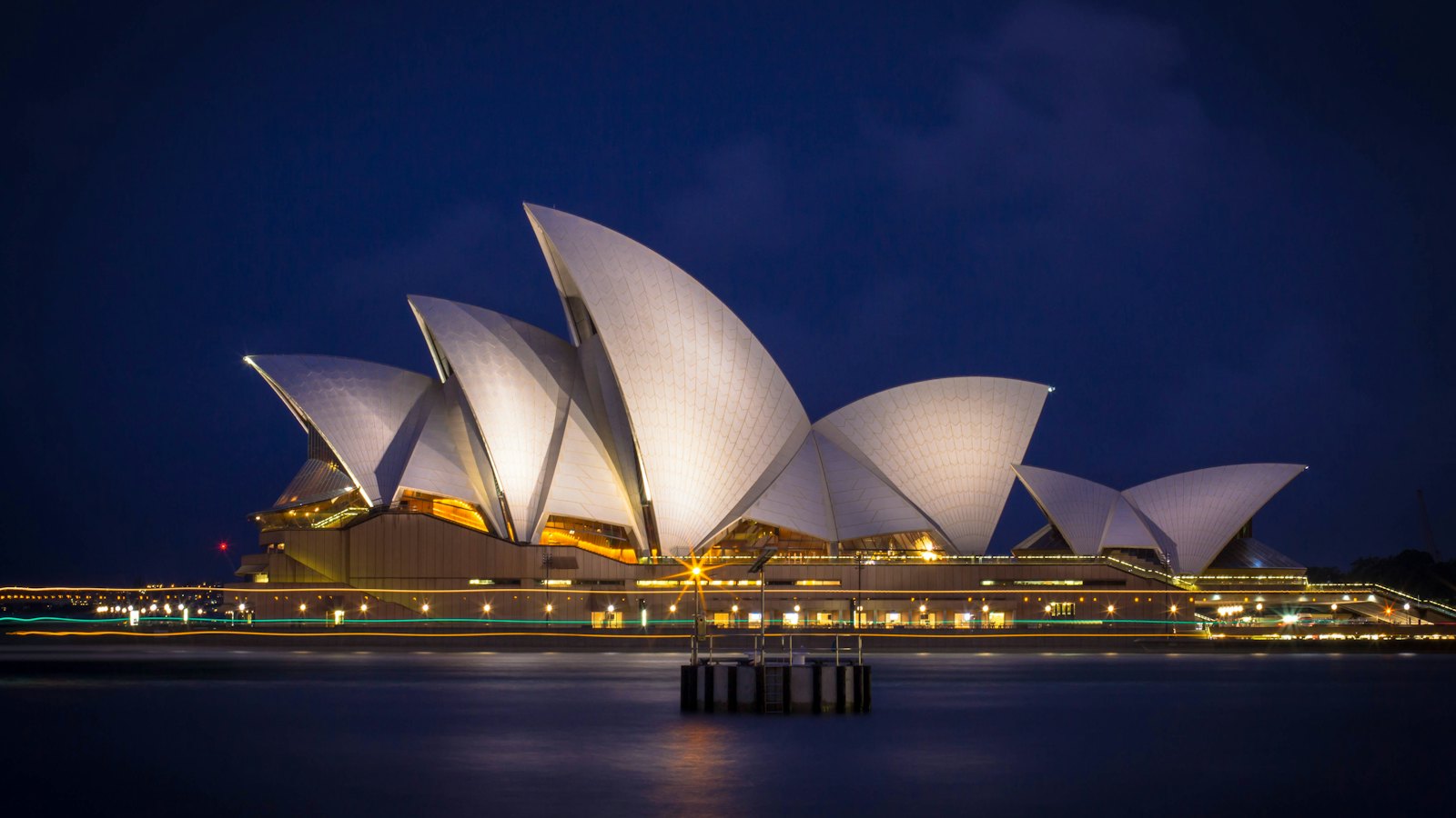 Sydney Opera House sails lit at blue hour above calm Sydney Harbour, Australia