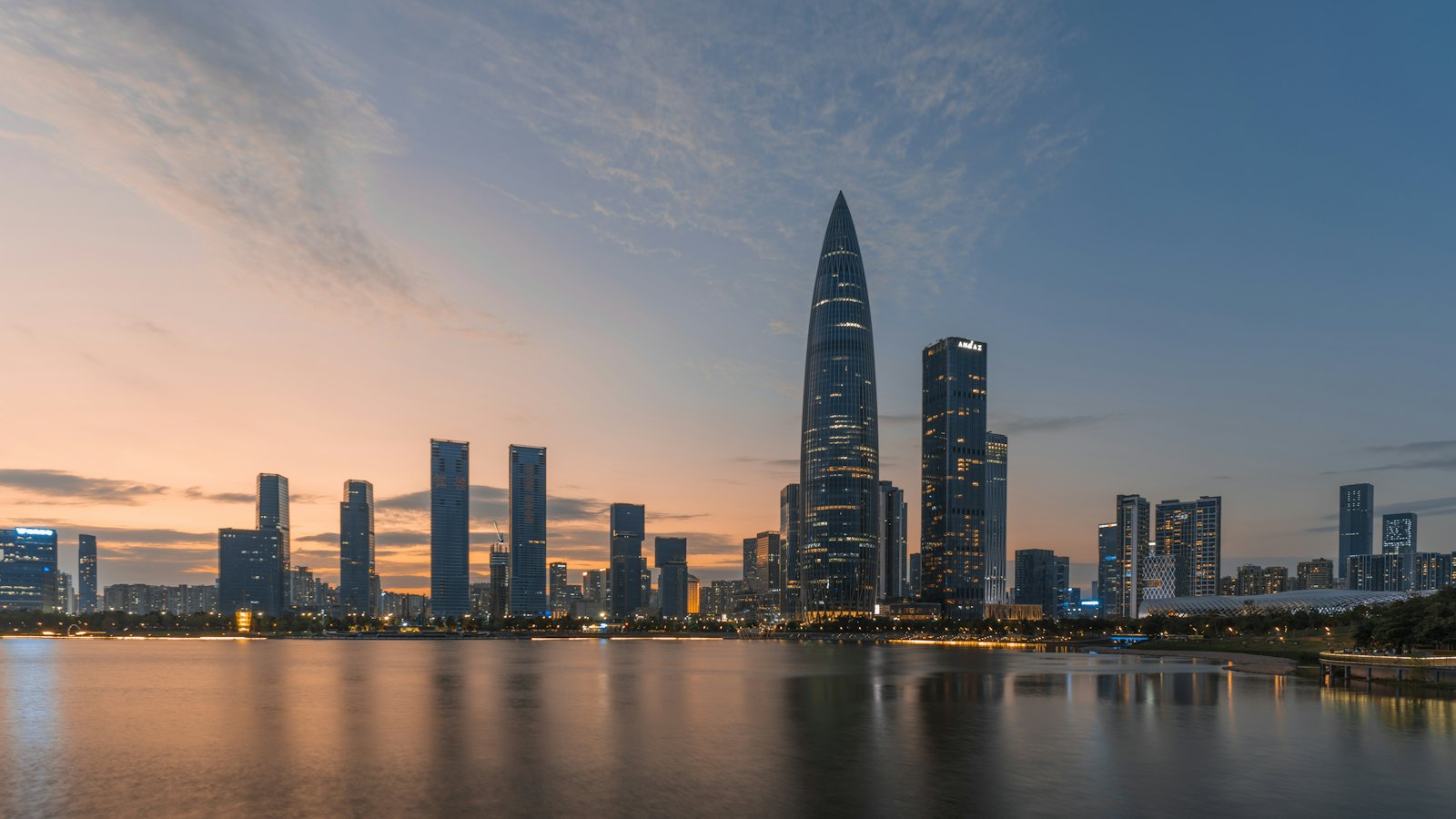 China Resources Tower rising over Shenzhen Bay's Houhai skyline at dusk, reflected in calm water