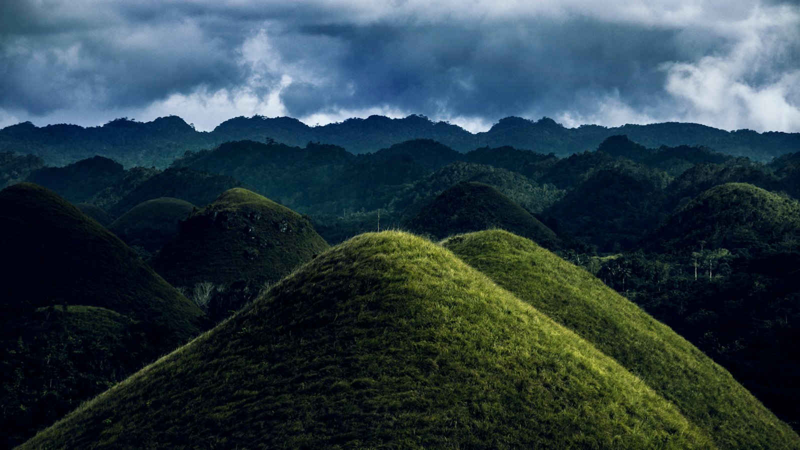 Cone-shaped Chocolate Hills rolling into the distance under a moody stormy sky