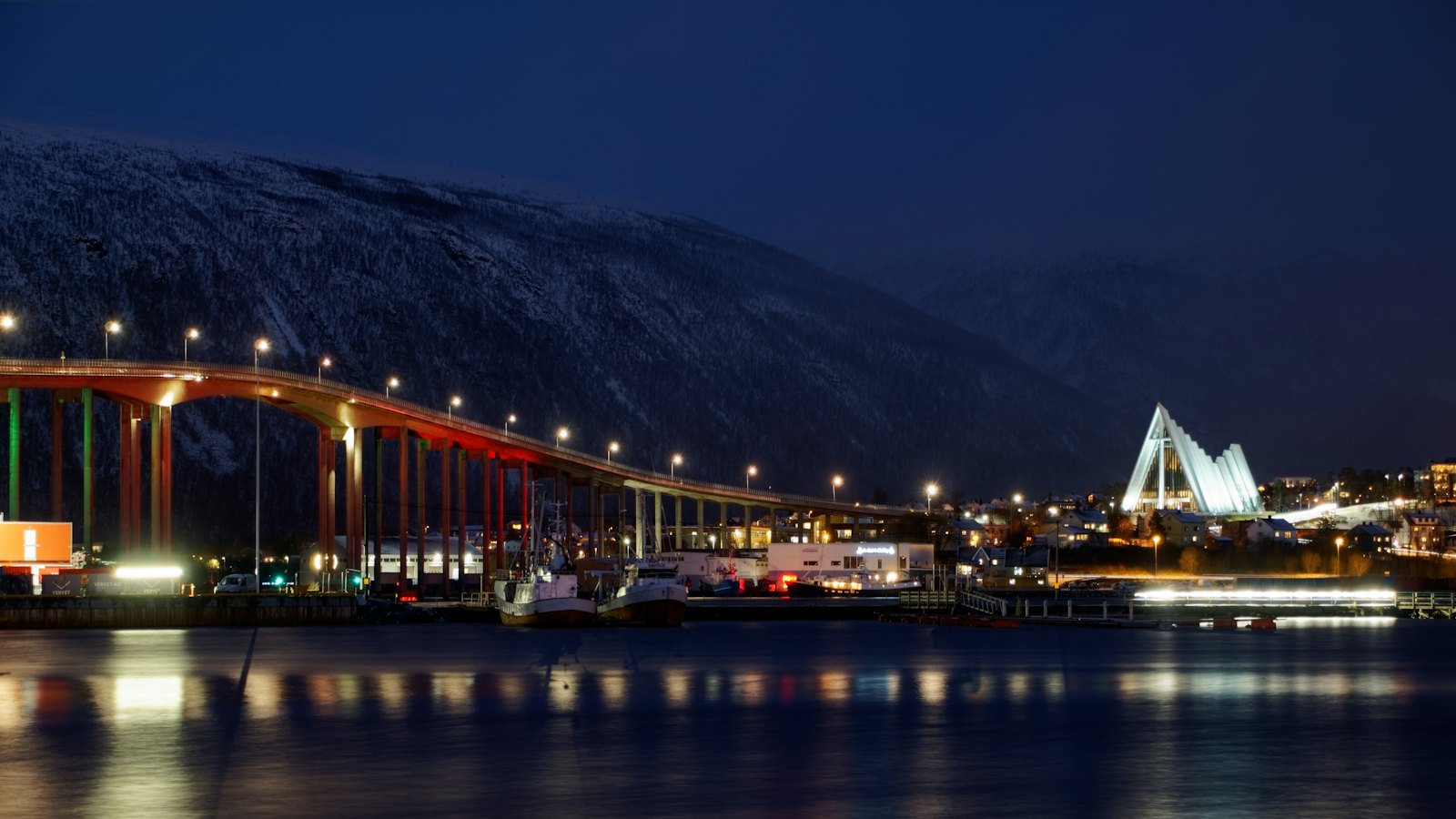 The illuminated Tromso Bridge and Arctic Cathedral glowing beside the fjord at night