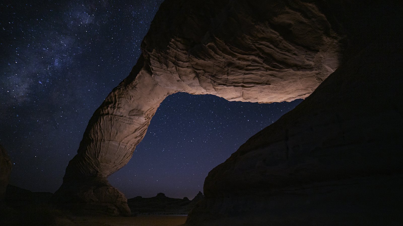 Natural sandstone rock arch silhouetted against a starry night sky in AlUla