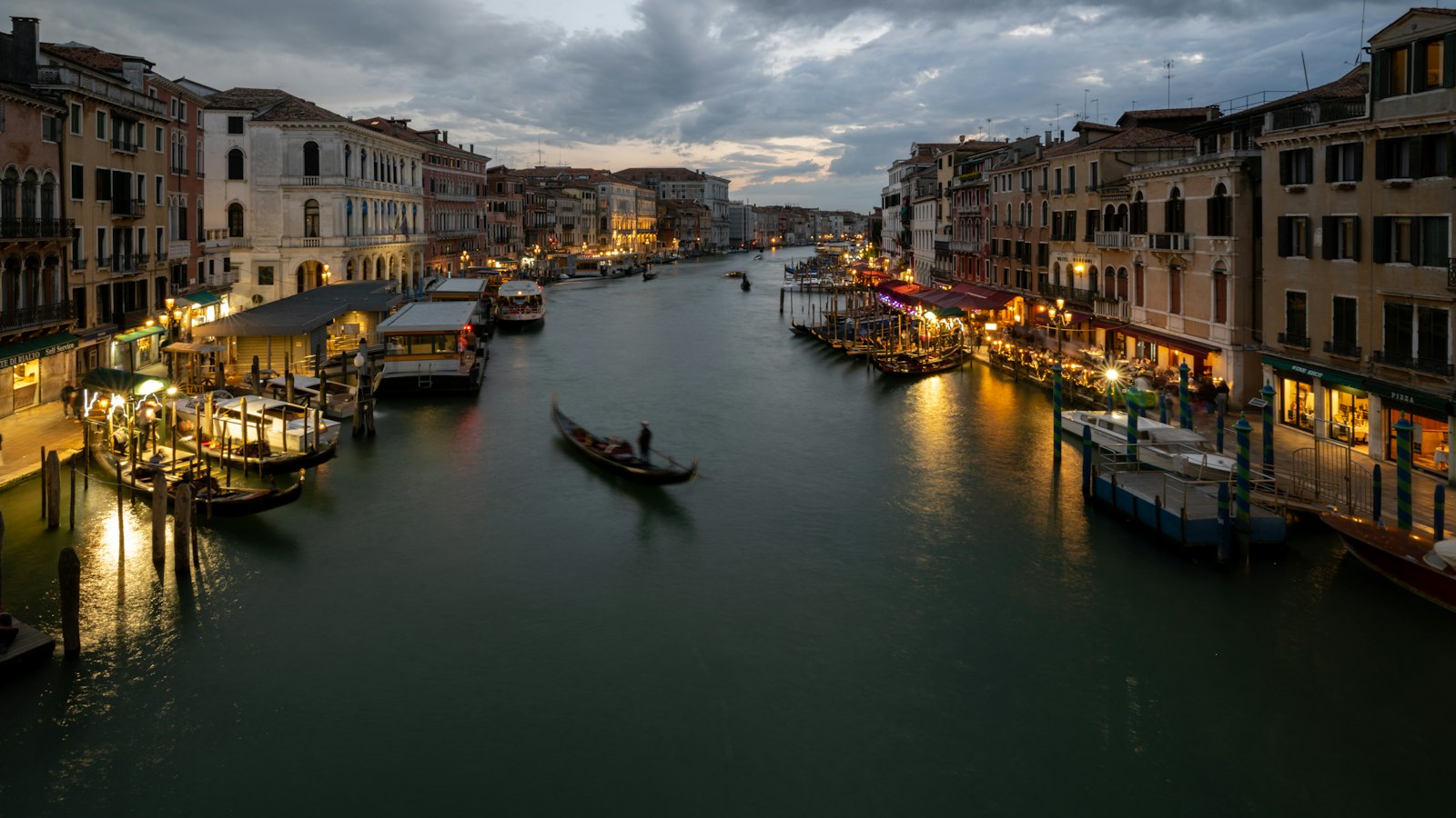 A gondola crossing Venice's Grand Canal at dusk beneath a moody sky