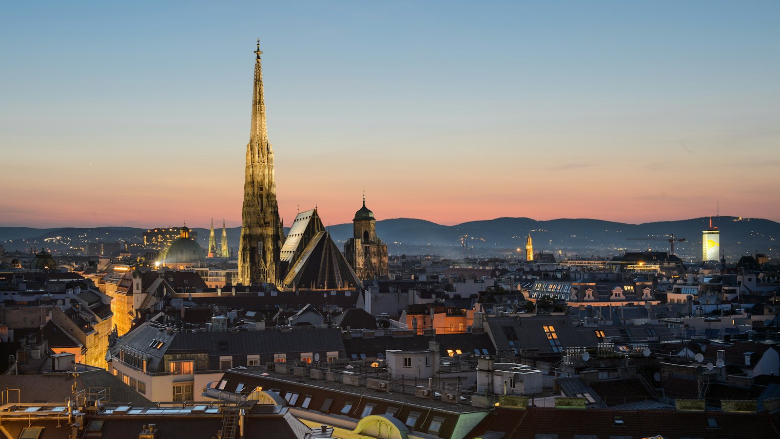St. Stephen's Cathedral spire rising above Vienna's old town rooftops at dusk with hills beyond