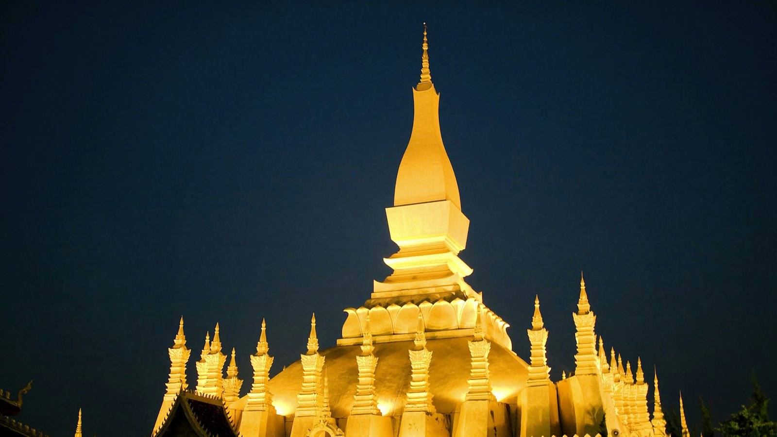 Pha That Luang golden stupa in Vientiane, Laos, floodlit against a deep blue night sky