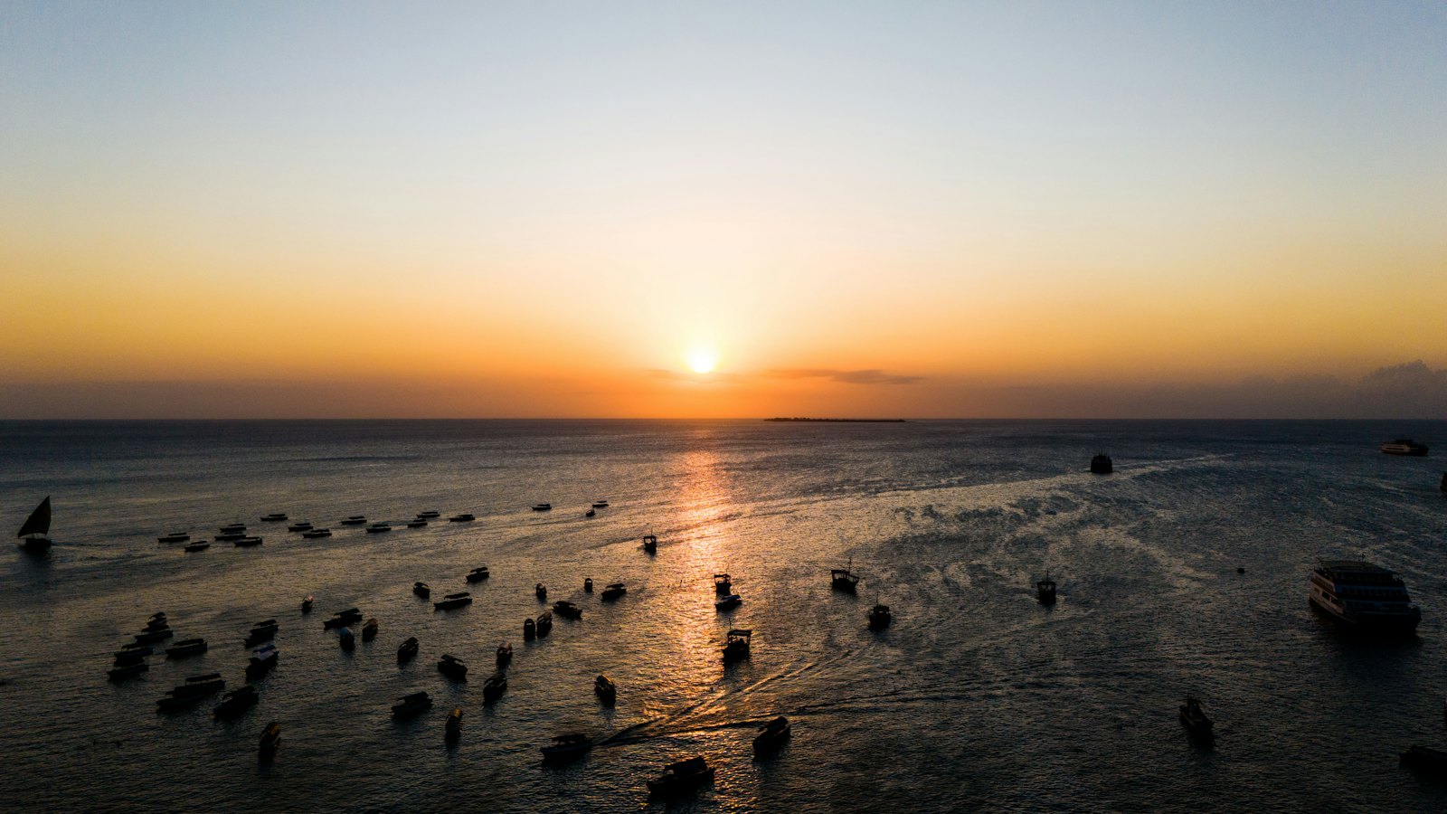 Traditional dhow boats scattered across Stone Town's harbour at sunset in Zanzibar