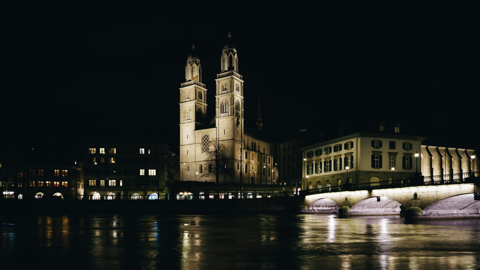 Grossmünster twin towers floodlit at night above the dark Limmat river in Zurich